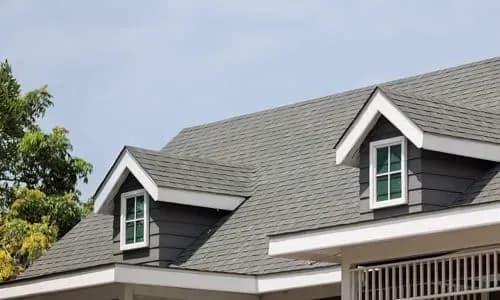 Dark architectural shingle roof with twin dormers, seen against a clear sky